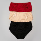 Three pairs of women's high-waisted briefs stacked vertically on a beige burlap background. The top pair is red with floral lace detailing, the middle is beige with lace detailing, and the bottom is black with lace detailing.